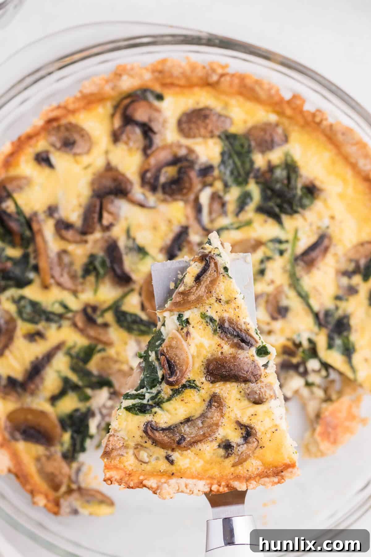 Earthy Mushroom and Fresh Spinach Quiche 8 A single slice of Spinach Mushroom Quiche being lifted from the pie pan with a serving spatula, showcasing its golden crust and creamy, veggie-filled interior.