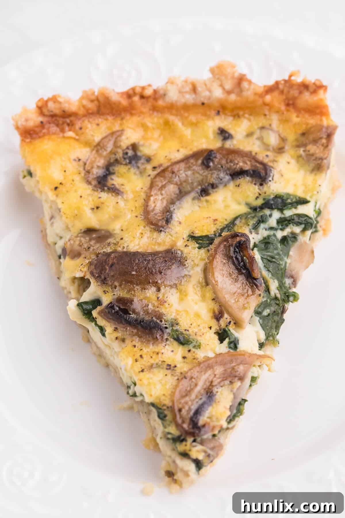 Earthy Mushroom and Fresh Spinach Quiche 9 A perfectly portioned slice of Spinach Mushroom Quiche on a white plate, with the creamy filling and visible vegetables showcased. The golden-brown crust adds to its inviting appeal.
