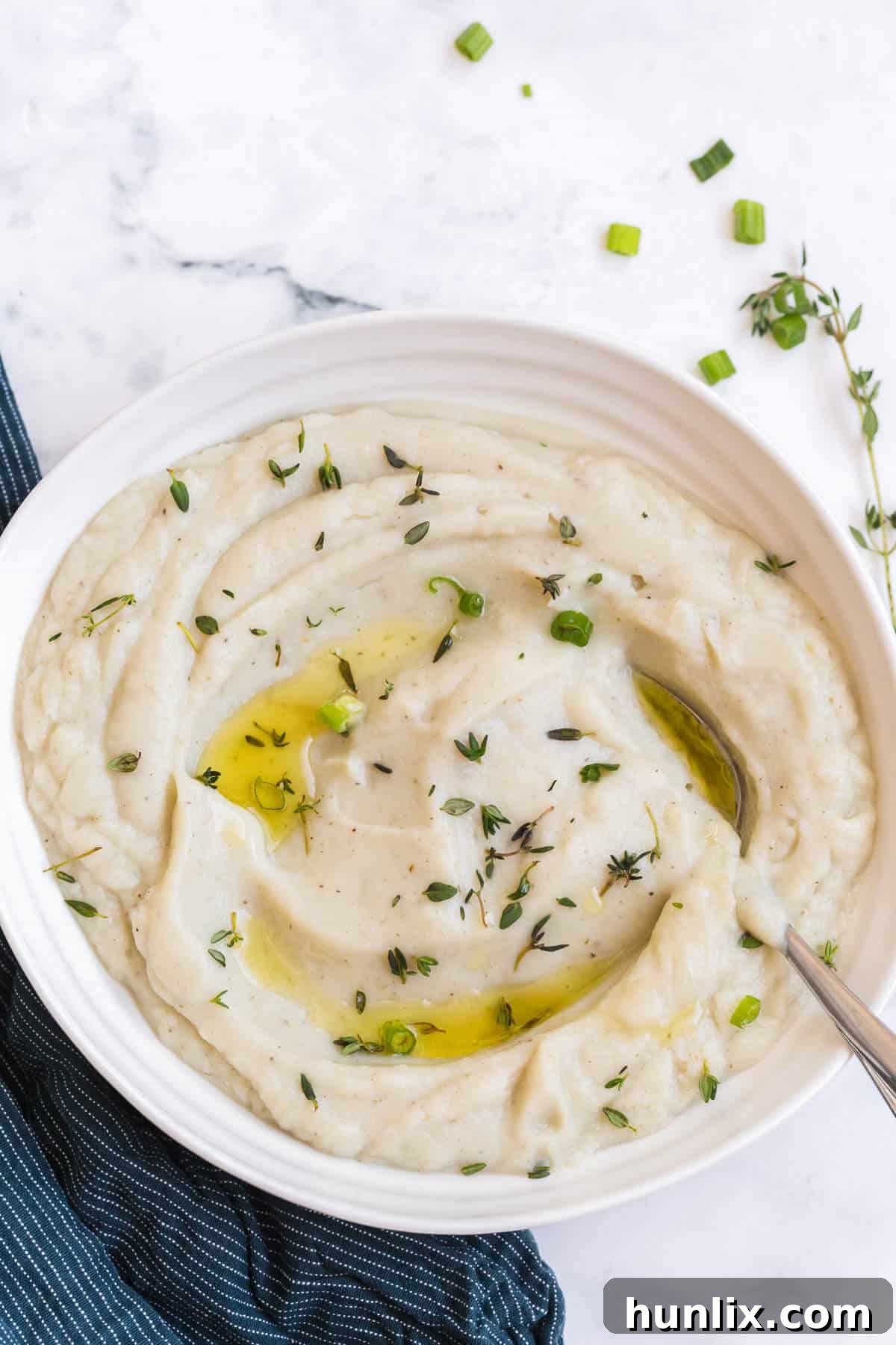 Creamy Vegan Cauliflower Mash 2 A bowl of creamy, white vegan mashed cauliflower, garnished lightly and ready to be served. A spoon is resting in the bowl.