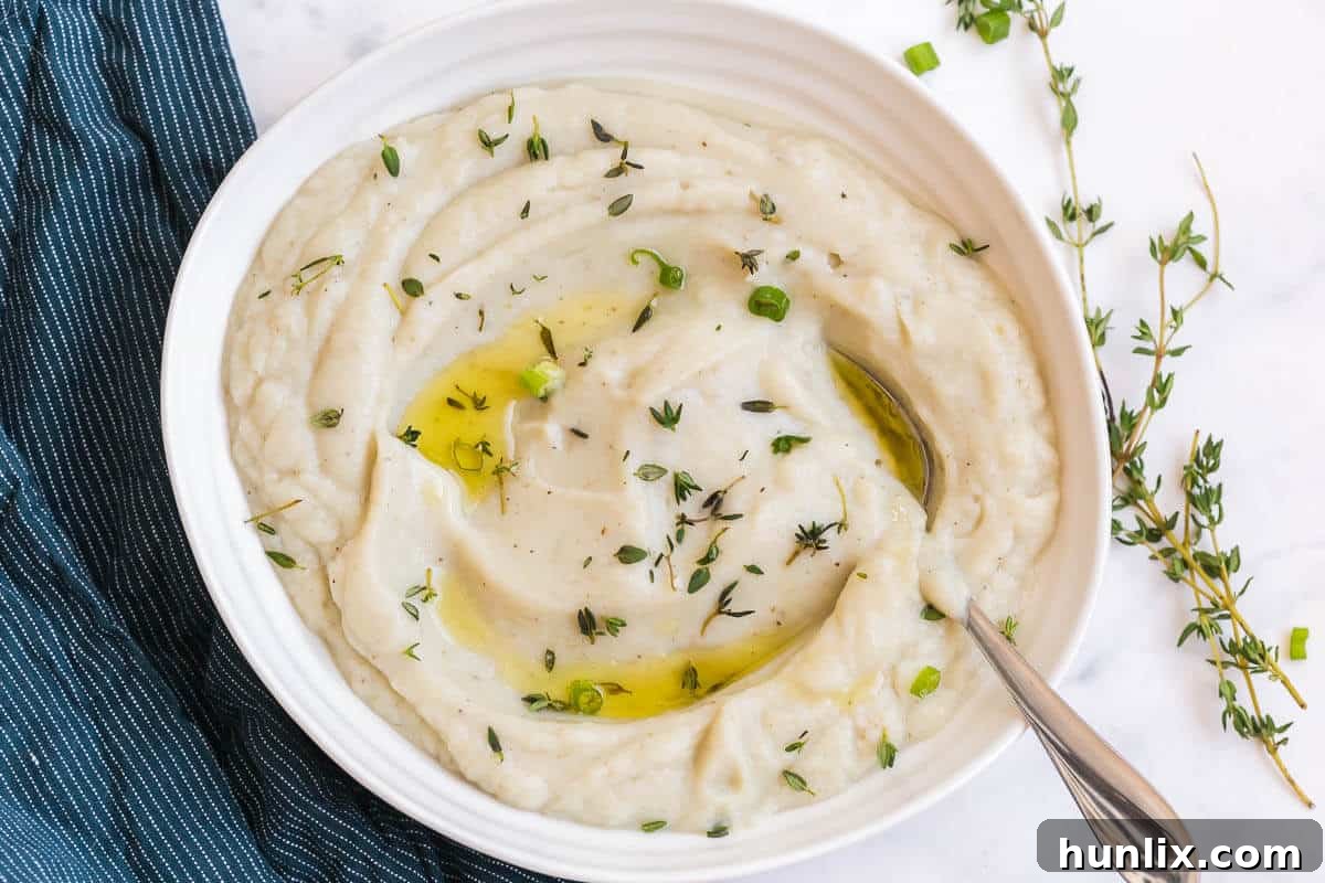 Creamy Vegan Cauliflower Mash 3 A close-up shot of creamy vegan mashed cauliflower in a white bowl with a serving spoon, highlighting its smooth texture and inviting appearance.