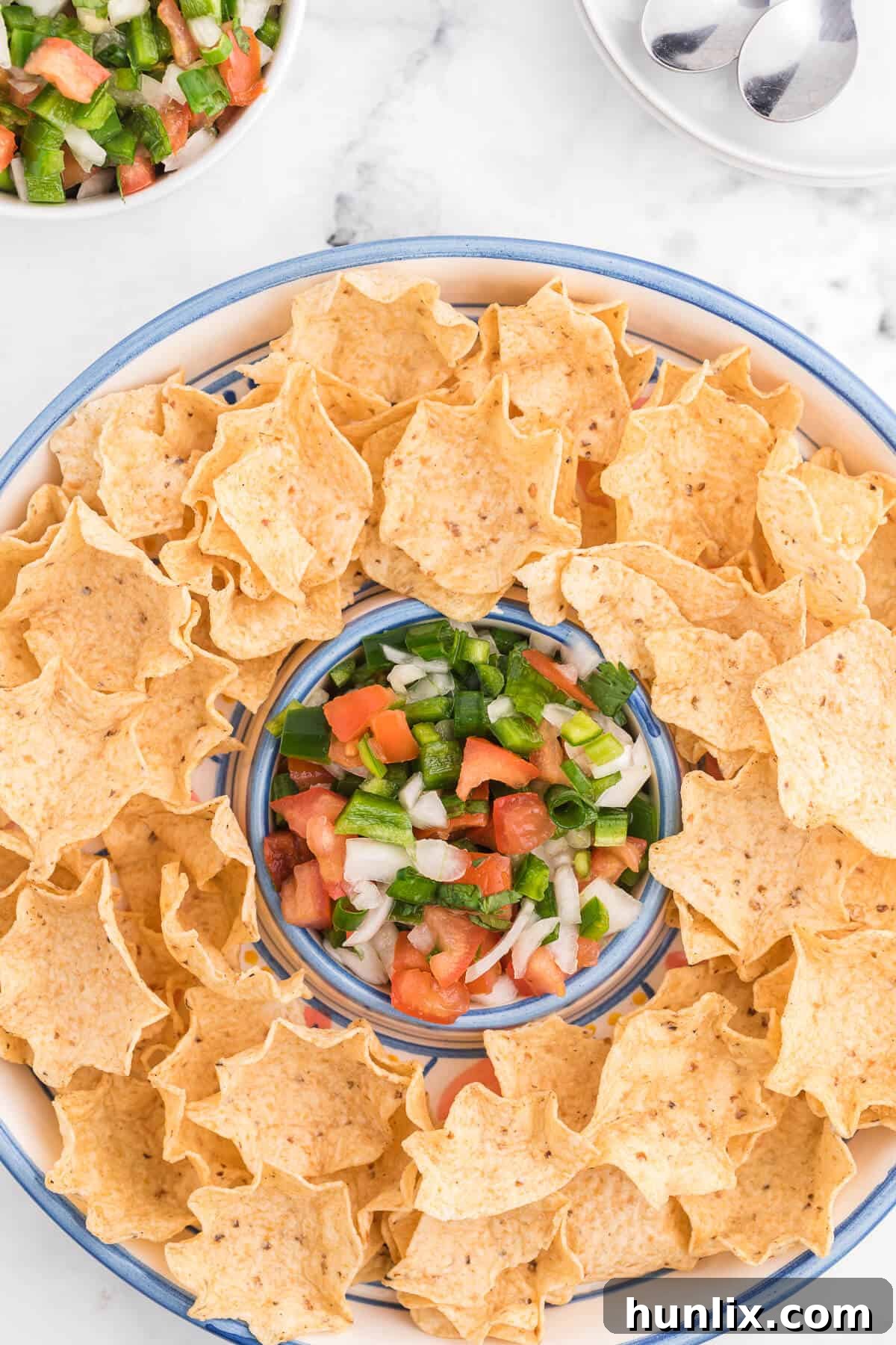 A platter of golden tortilla chips arranged around a vibrant bowl of homemade Pico de Gallo, showcasing its fresh ingredients and inviting colors.