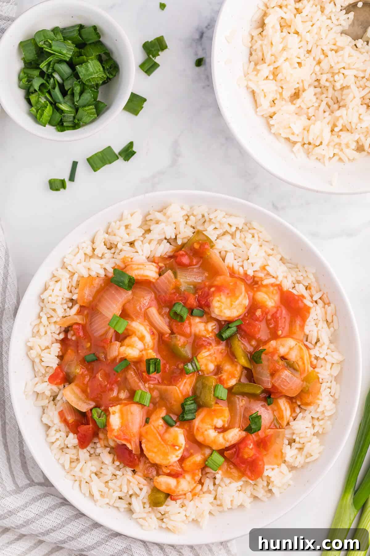 A serving of Shrimp Creole nestled over fluffy white rice in a white bowl, garnished with fresh green onions.