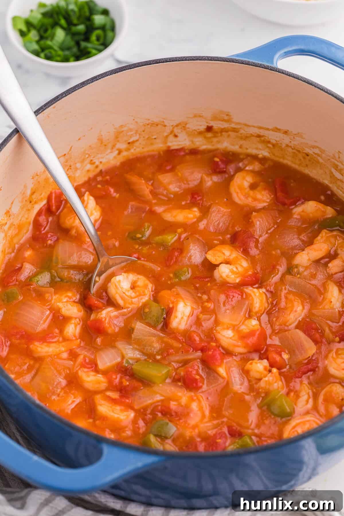 Shrimp Creole simmering in a blue Dutch oven with a serving spoon, showcasing its rich, thick tomato sauce and succulent shrimp.