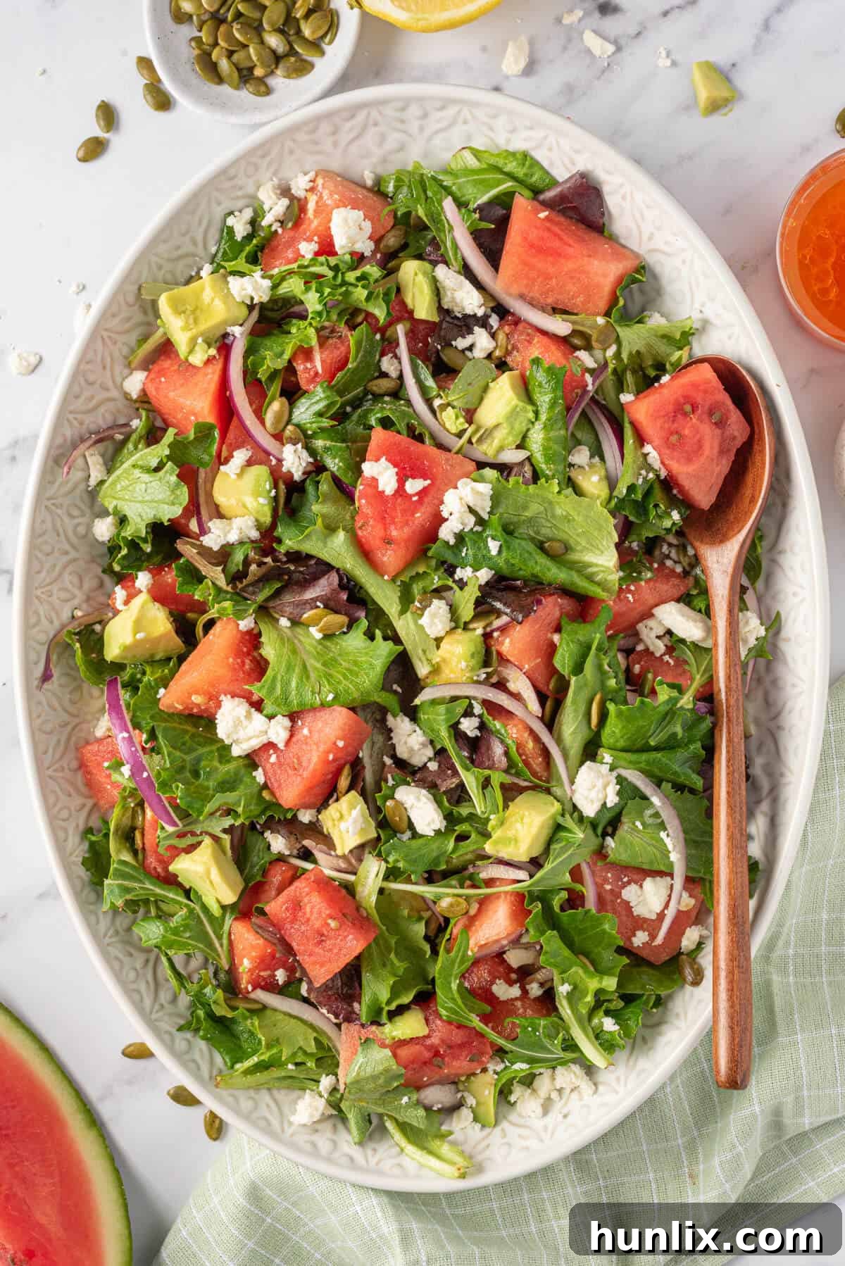 Watermelon and feta salad artfully arranged on a pristine white platter with a serving spoon, highlighting its vibrant colors and fresh ingredients.