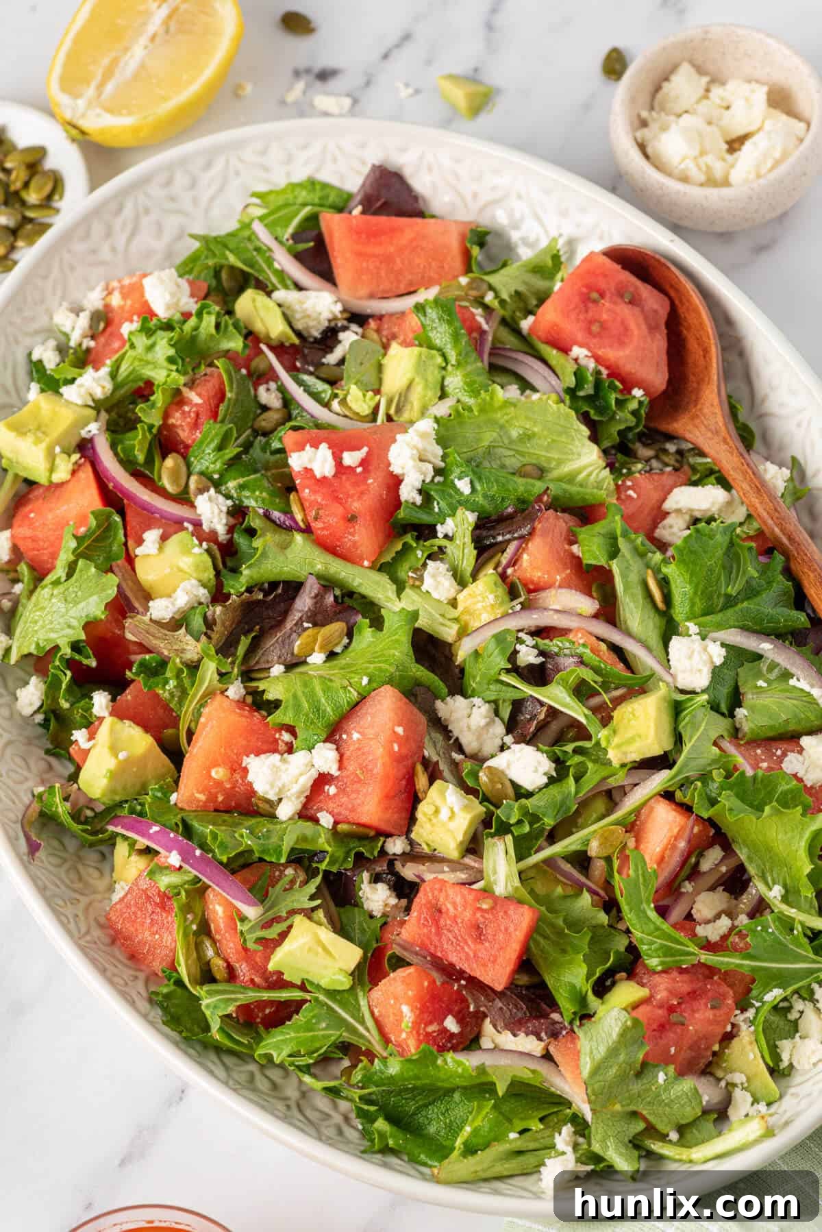 A white platter generously filled with Watermelon and Feta Salad, featuring bright red watermelon chunks, white feta crumbles, and green avocado, presented beautifully for serving at a summer gathering.