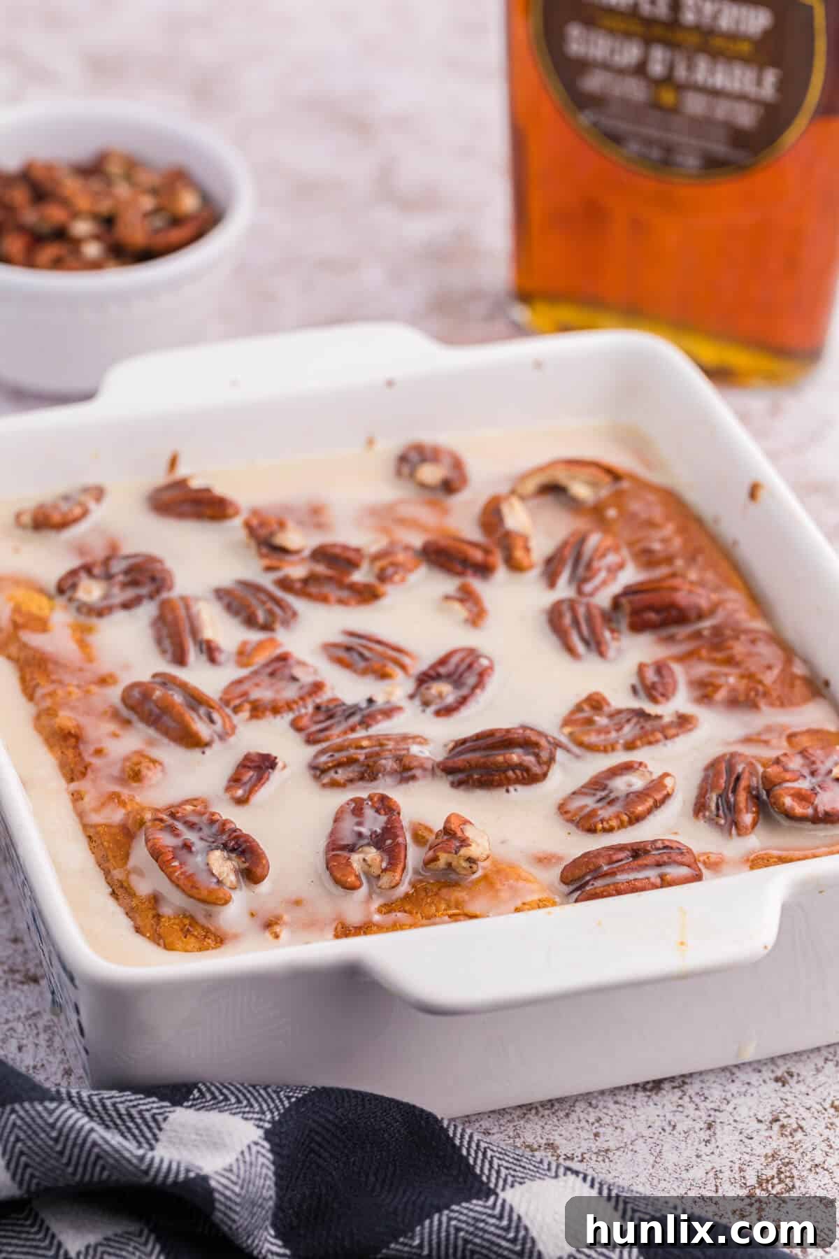 A golden-brown maple pecan danish bake in a casserole dish, topped with a creamy maple glaze and whole pecans.