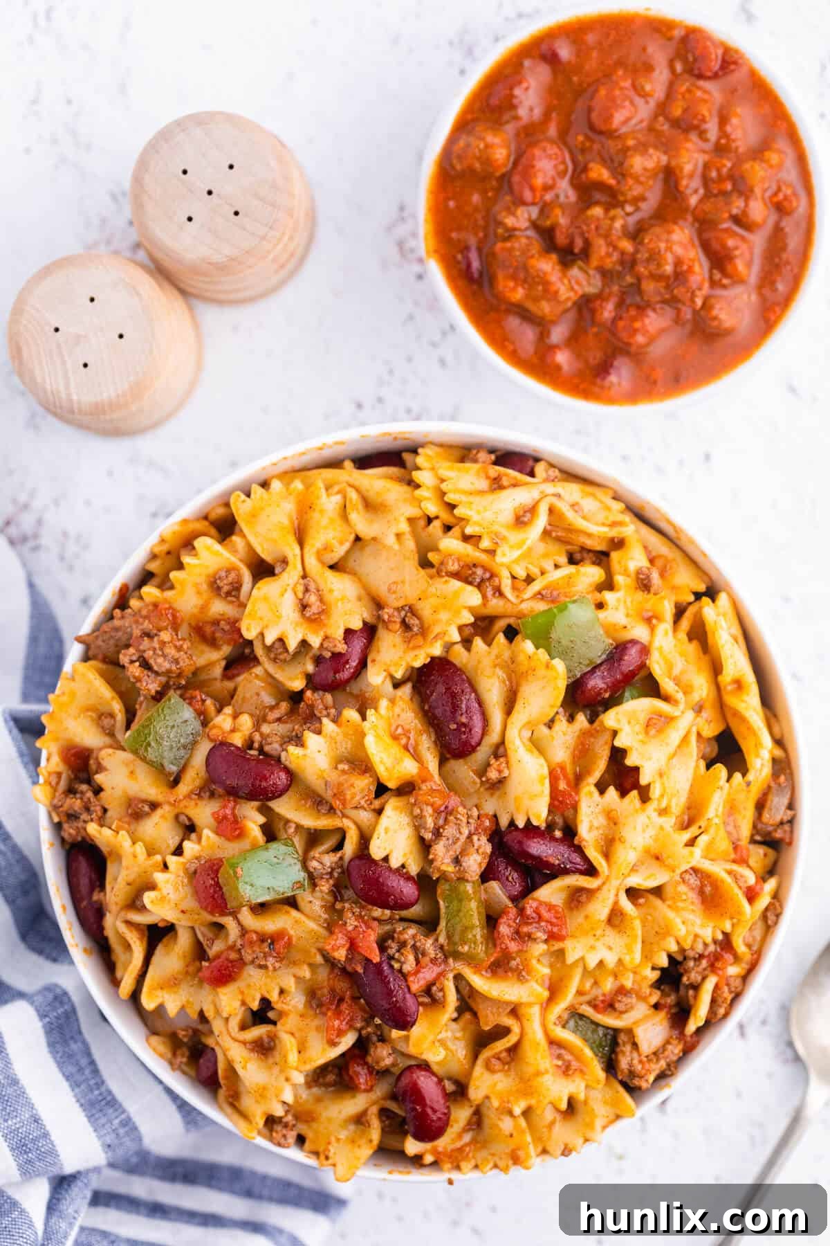 A large bowl of vibrant Chili Pasta Salad, ready to be served, showcasing tender bowtie noodles mixed with a rich, spicy chili base, garnished with fresh herbs.