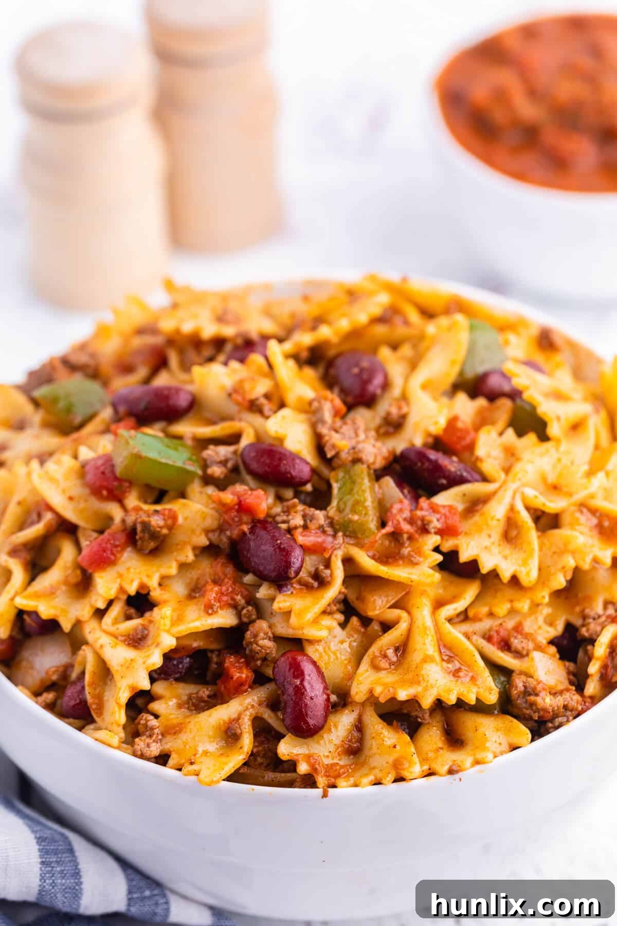 A close-up shot of Chili Pasta Salad in a pristine white bowl, garnished with a sprig of fresh cilantro, emphasizing its vibrant colors and inviting textures.