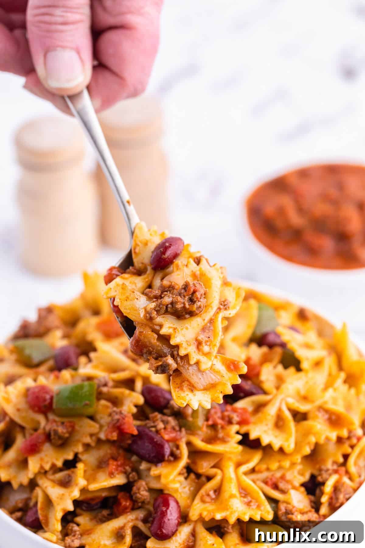 A serving spoon lifting a portion of Chili Pasta Salad from a bowl, showcasing the rich colors and textures of the dish.