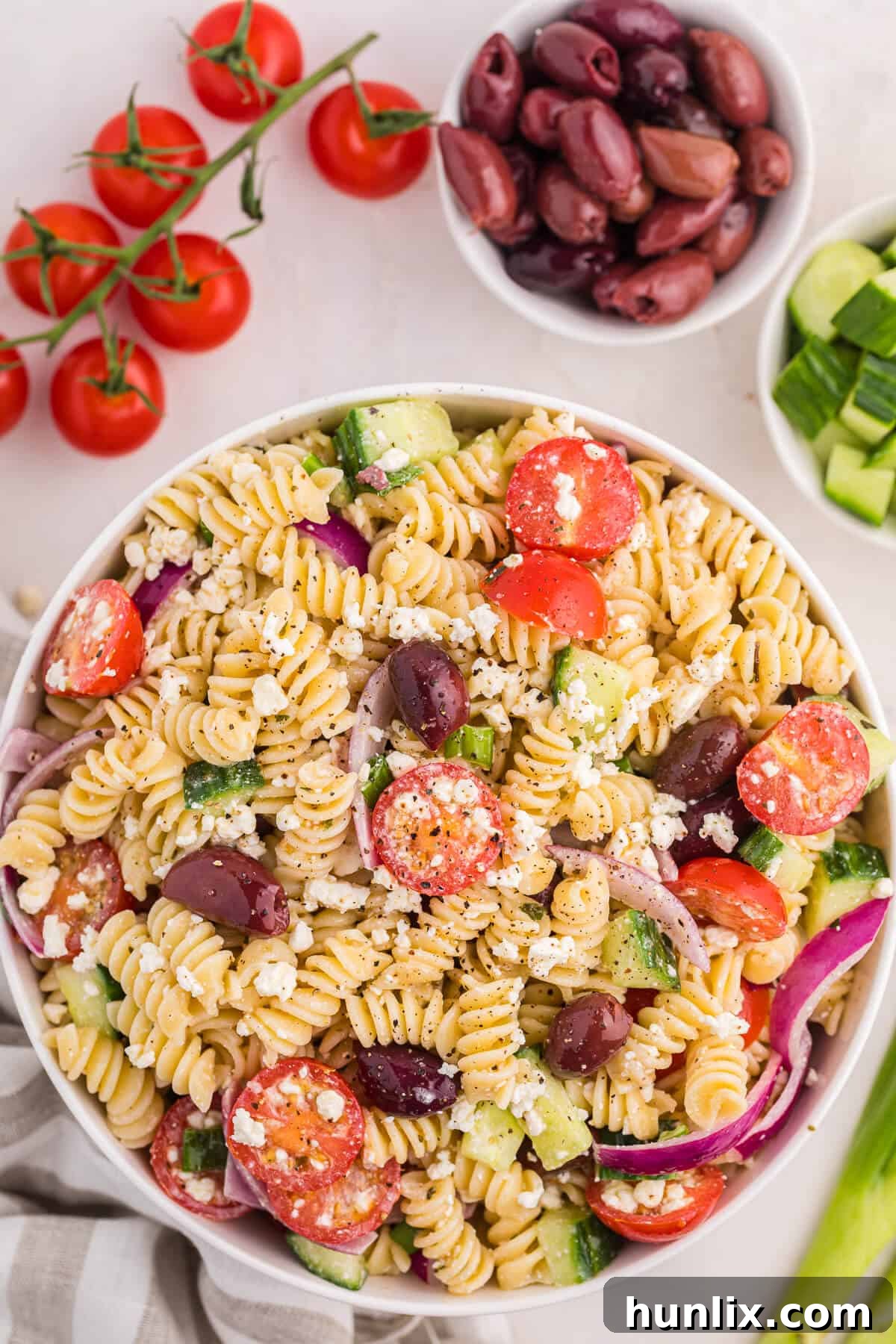 Zesty Greek Pasta Medley 2 A vibrant bowl of Greek pasta salad, showcasing tender pasta, black olives, halved cherry tomatoes, sliced cucumbers, and crumbled feta cheese, ready to be served as a refreshing summer dish.