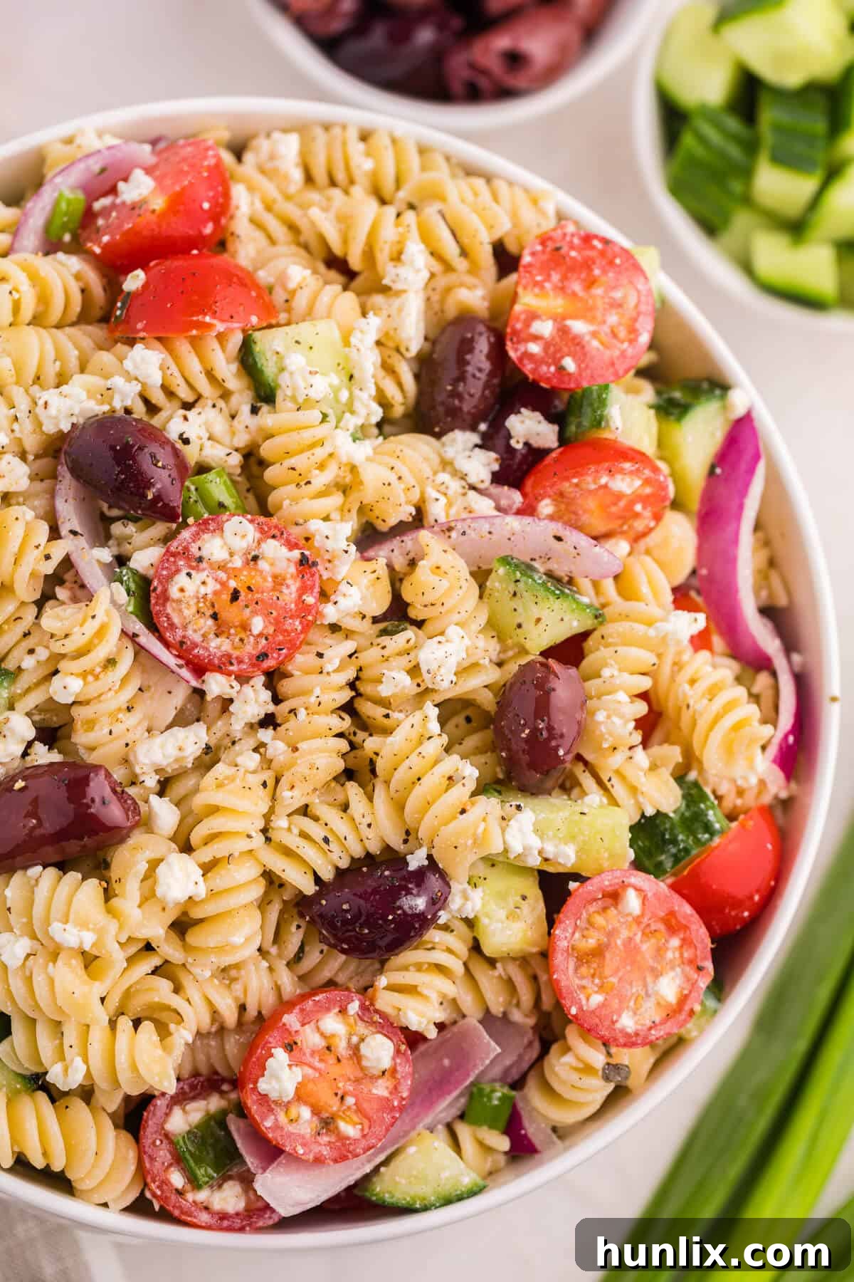 Zesty Greek Pasta Medley 7 A large glass bowl of Greek pasta salad, showcasing the colorful mix of pasta, olives, tomatoes, cucumbers, and feta cheese, ready for serving or storage.
