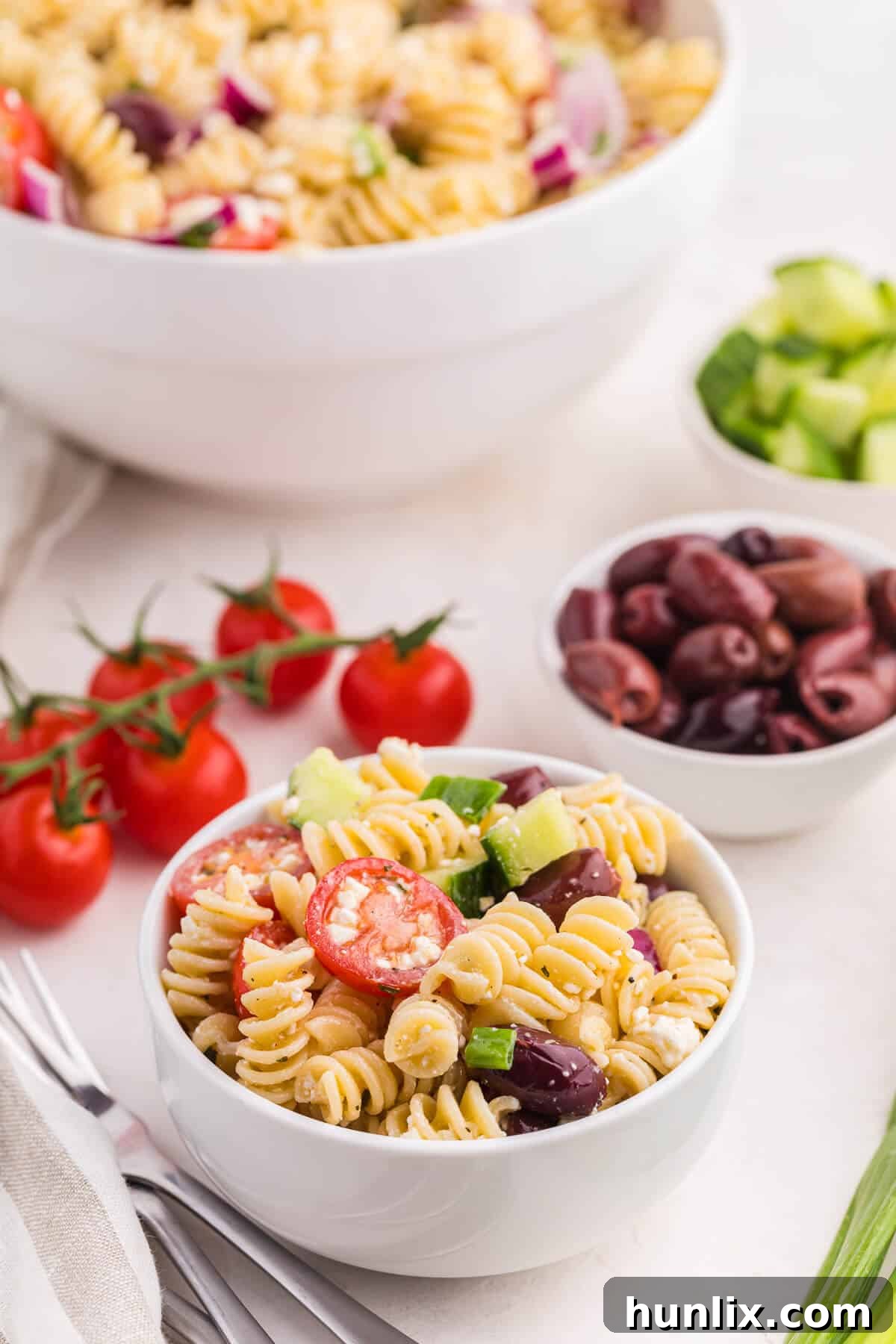 Zesty Greek Pasta Medley 9 A small white bowl filled with Greek pasta salad, garnished with a sprig of fresh dill, presented on a light wooden surface.