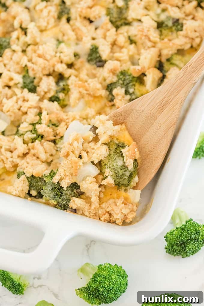 A close-up of the baked broccoli casserole in a white pan with a wooden serving spoon, showing the crispy topping and creamy interior.