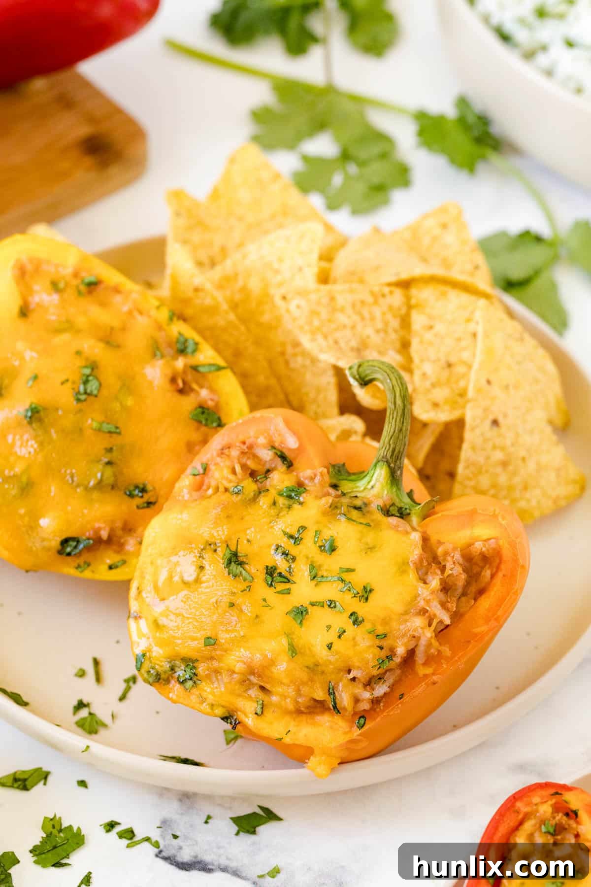 Two halves of Mexican stuffed peppers on a plate, garnished with cilantro, next to tortilla chips.