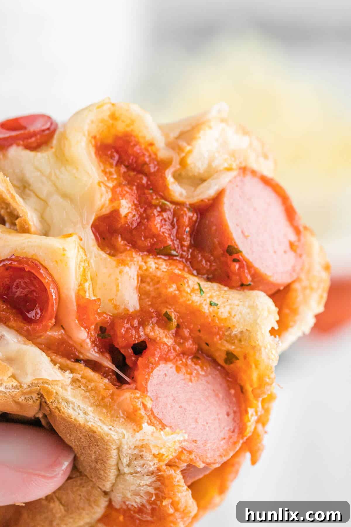 Pizzadog 7 A hand holding a pizza hot dog, cut in half to show the melted cheese and toppings.