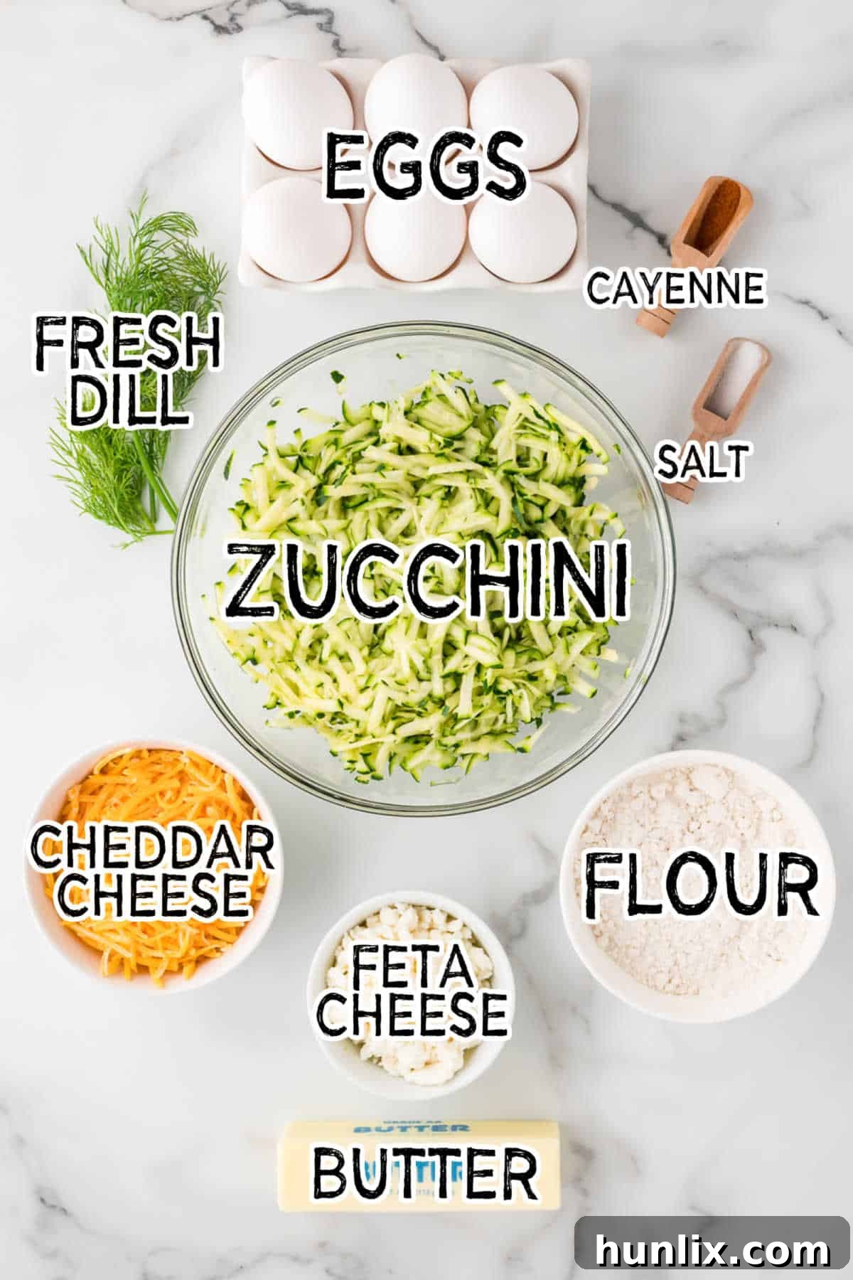 Close-up of fresh ingredients for Cheesy Zucchini Bake: zucchini, eggs, dill, feta cheese, cheddar cheese, flour, butter, salt, and cayenne pepper.
