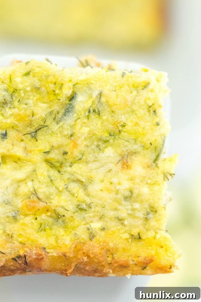 A close-up shot of a slice of Cheesy Zucchini Bake on a plate, showing the layers of cheese and zucchini.