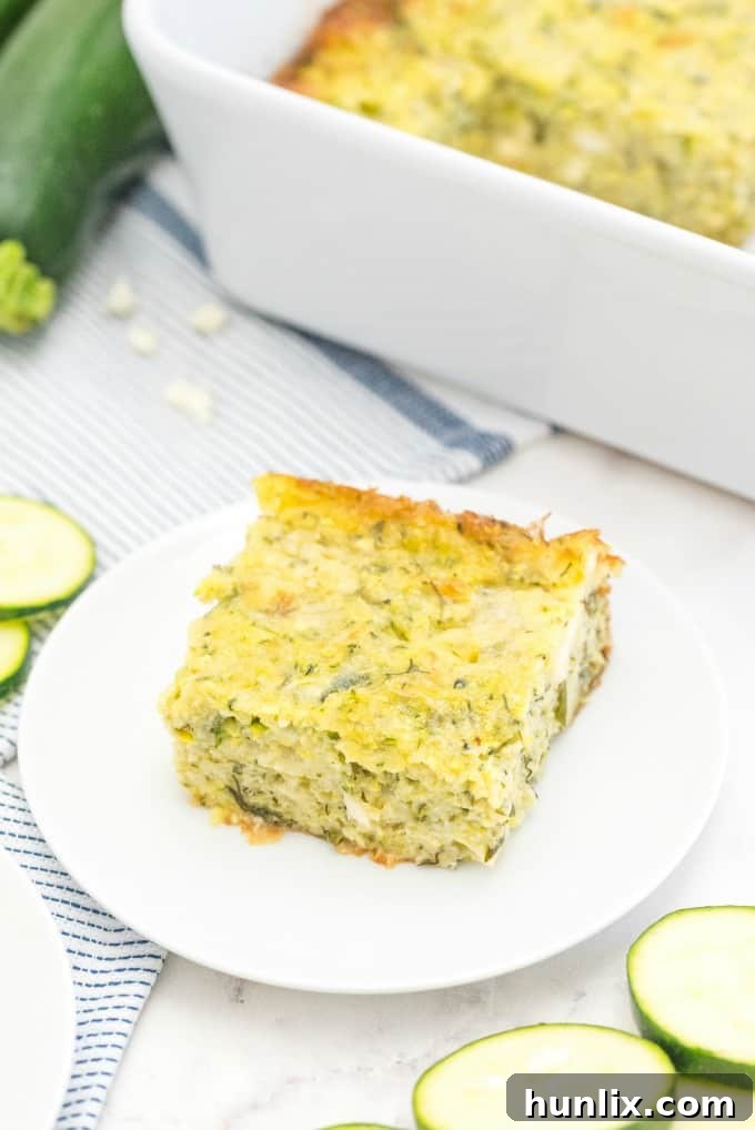 A close-up of a perfectly baked square slice of Cheesy Zucchini Bake, showcasing its golden-brown top and moist interior.