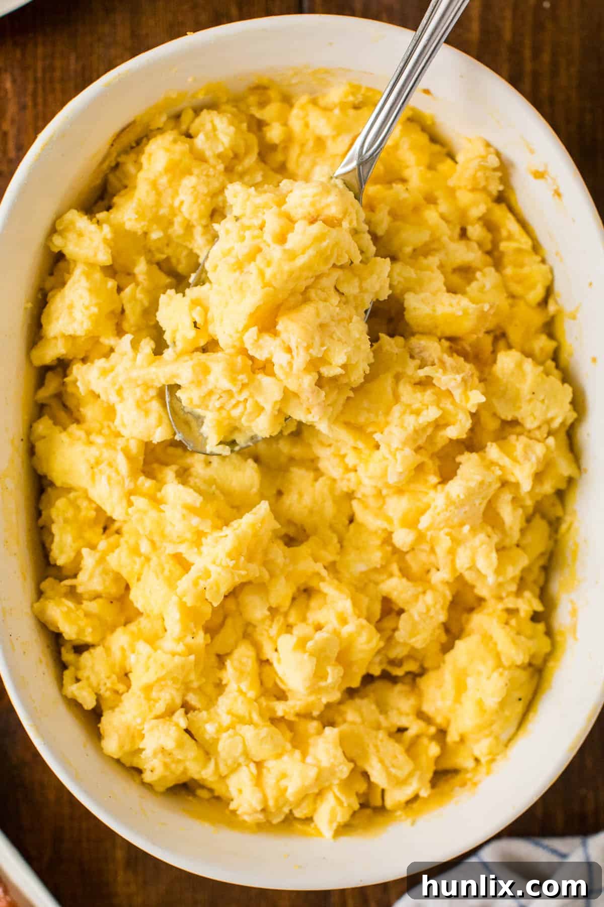 A large casserole dish filled with golden, fluffy oven scrambled eggs, with a serving spoon resting inside.