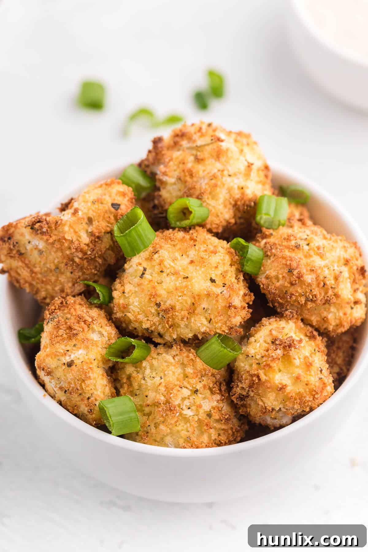 Freshly air-fried cauliflower bites, hot and crispy, presented in a rustic bowl on a wooden surface.
