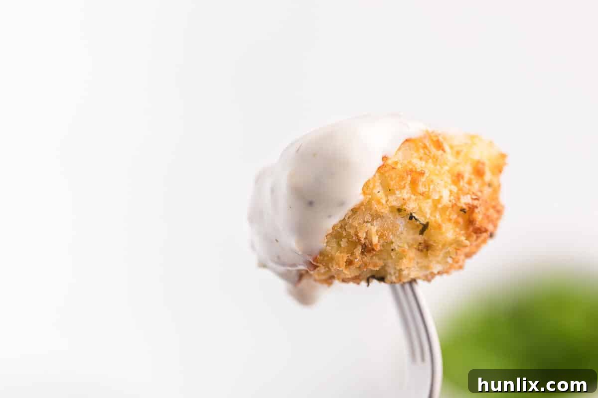 A single air-fried cauliflower bite, perfectly golden and crispy, held on a fork with a dollop of creamy ranch sauce.