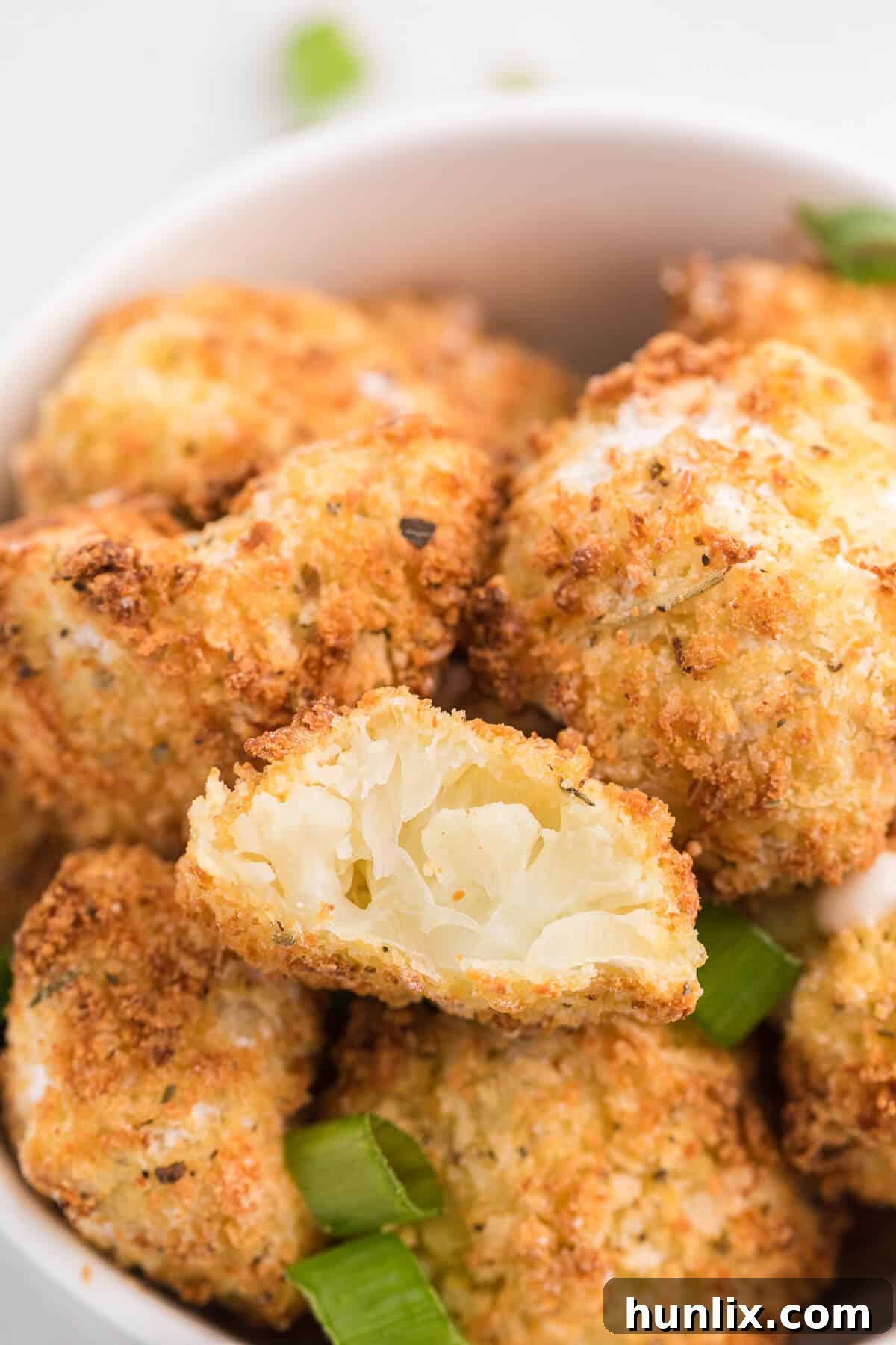 A bowl of hot Air Fryer Cauliflower Bites with one piece taken out, revealing the soft interior and crispy crust.