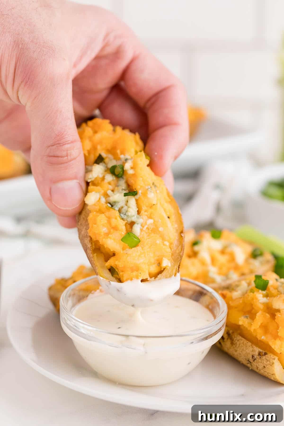 Buffalo Stuffed Potatoes 6 A hand dipping a Buffalo Twice-Baked Potato into a bowl of creamy ranch dip, highlighting its delicious appeal and perfect pairing.