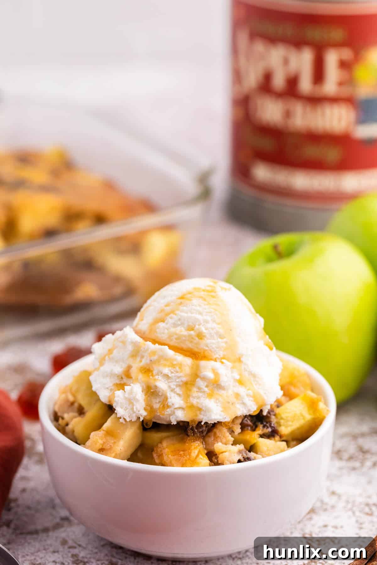 A close-up of a bowl of maple apple pudding, adorned with a swirl of vanilla ice cream and a drizzle of extra maple syrup.