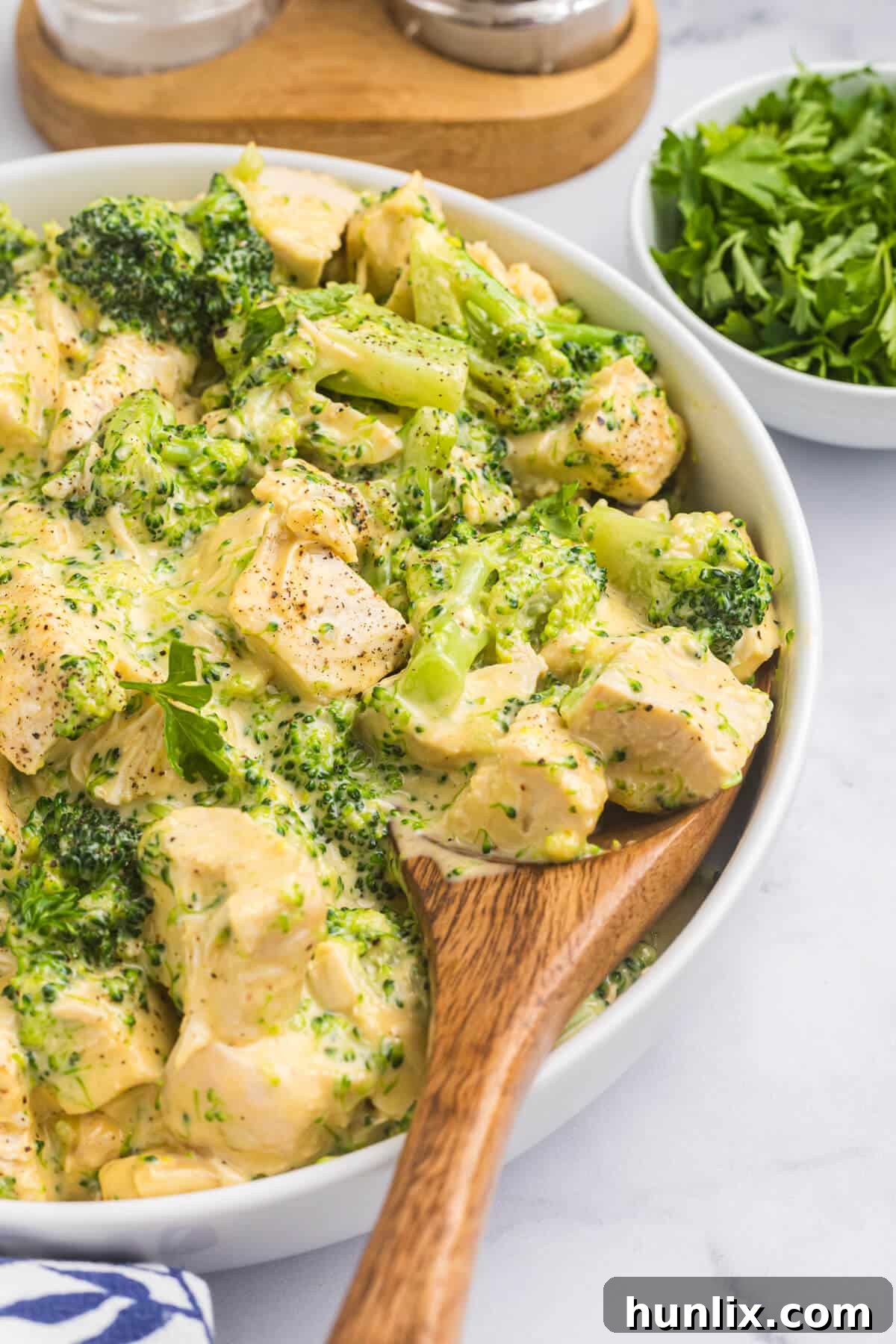 Ultimate Cheesy Chicken Broccoli Bake 5 Cheesy chicken and broccoli in a bowl with a wooden serving spoon.
