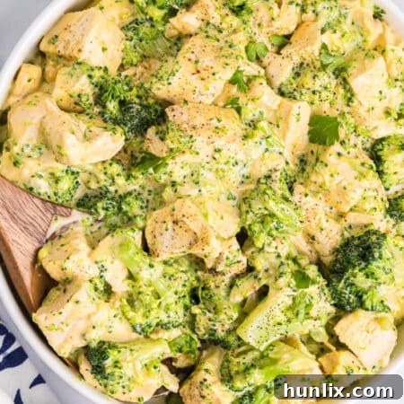 Ultimate Cheesy Chicken Broccoli Bake 8 Cheesy chicken and broccoli in a bowl with a wooden spoon.