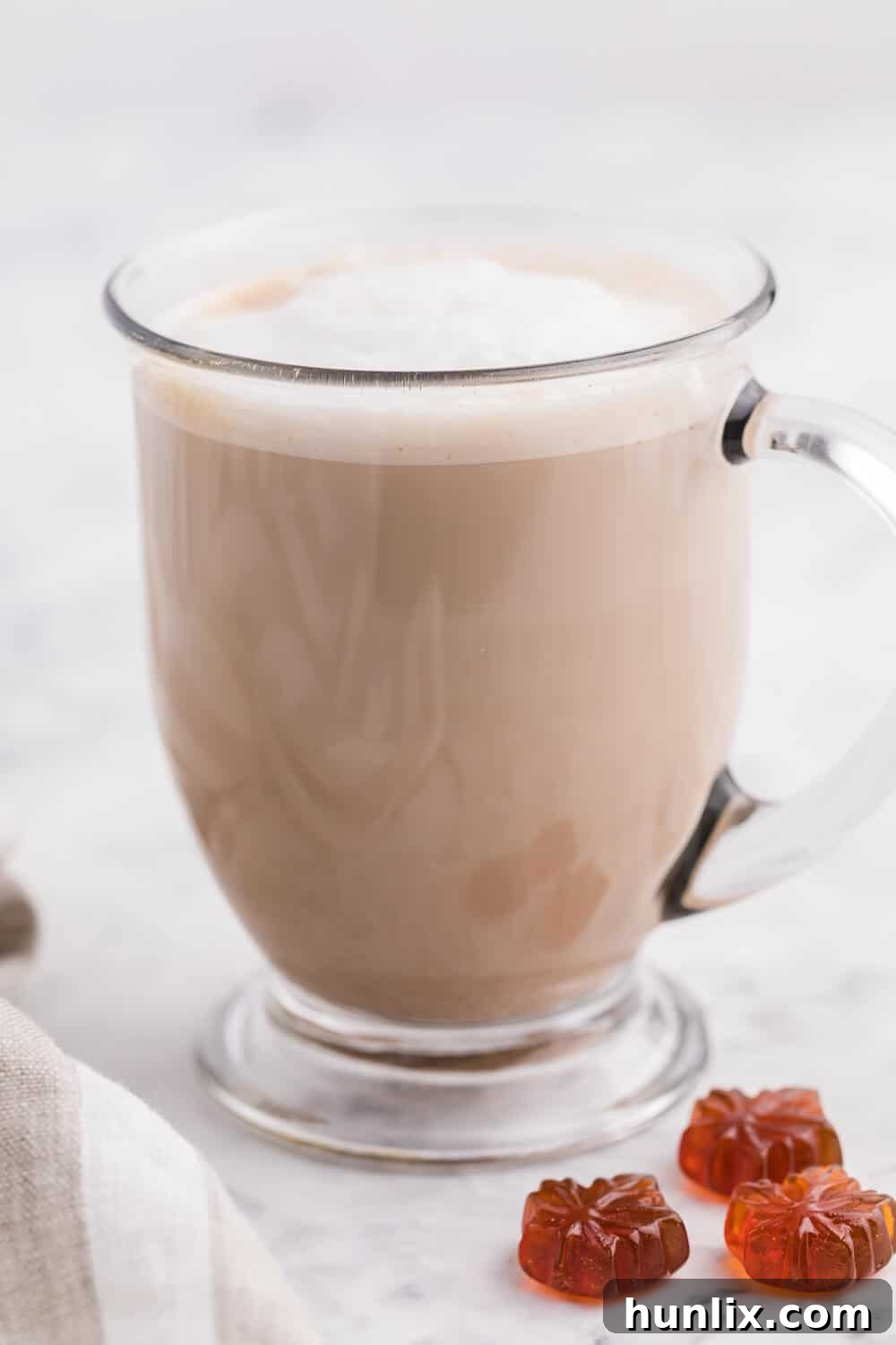 A close-up of a glass mug of maple latte, showing the frothy top and the warm beverage inside.