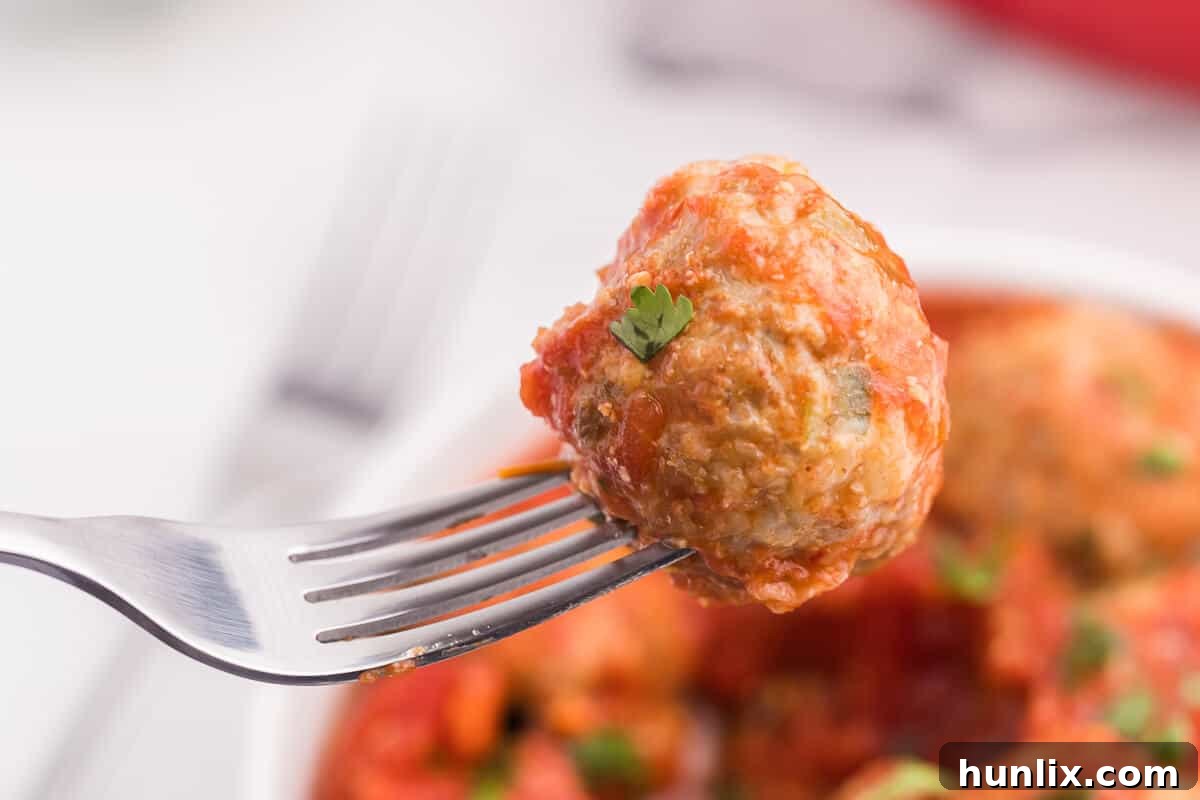 A single Mexican meatball, perfectly cooked and glistening with sauce, resting on a fork, ready to be tasted.