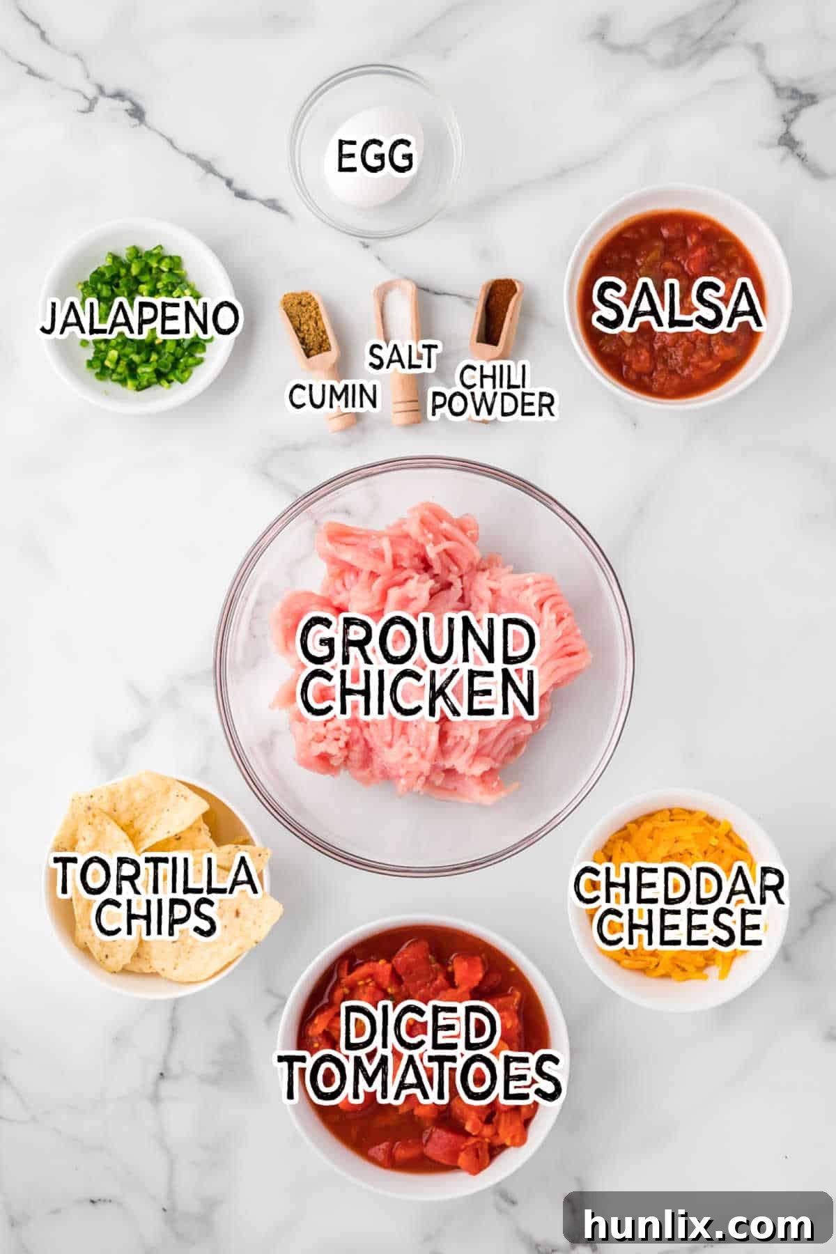 A vibrant collection of ingredients laid out on a table, including ground chicken, fresh jalapeño, spices, canned tomatoes, salsa, tortilla chips, cheddar cheese, and cilantro, ready to be transformed into Mexican meatballs.