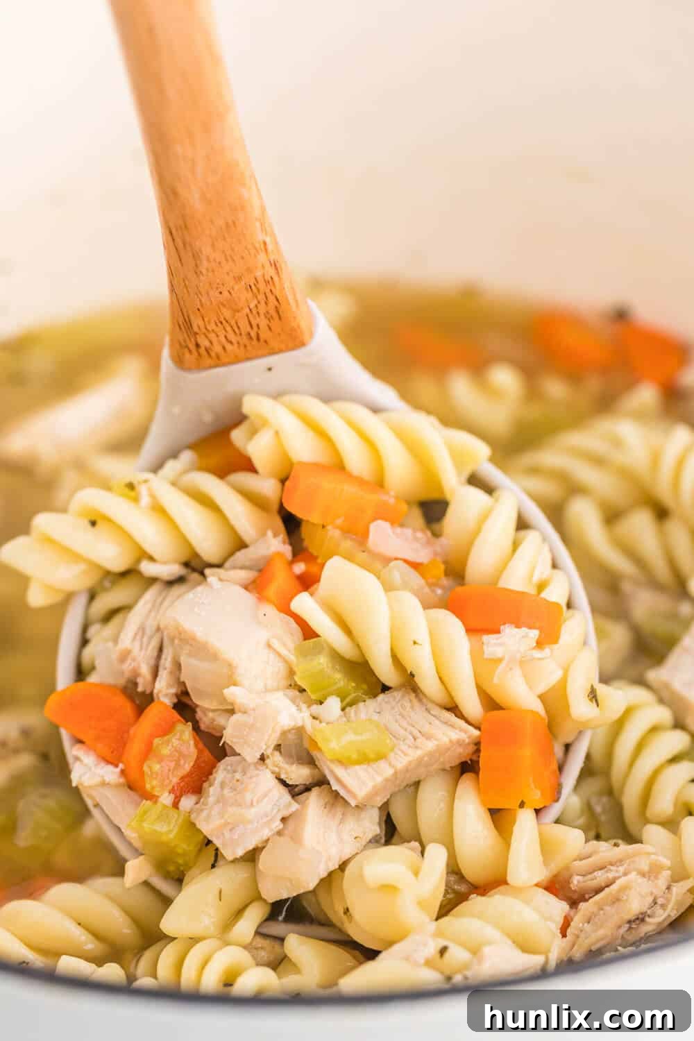 Grandma's Golden Chicken Noodle Soup 5 A ladle scooping steaming homemade chicken noodle soup from a large pot, showing the hearty contents.