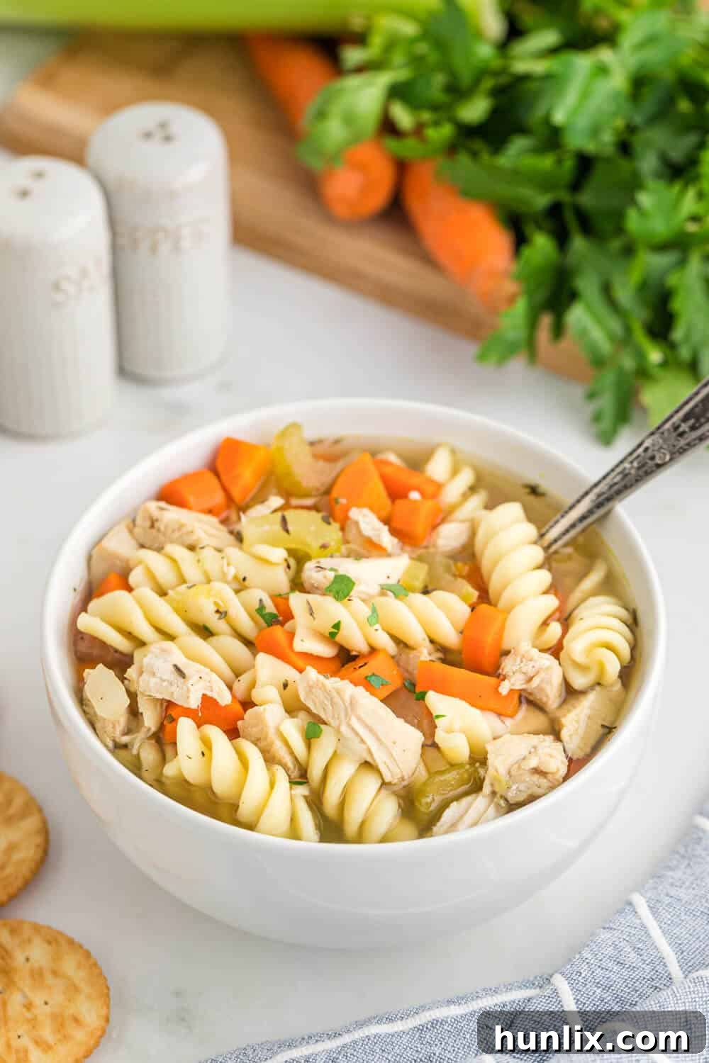 Grandma's Golden Chicken Noodle Soup 7 A bowl of homemade chicken noodle soup with a spoon in it, resting on a wooden surface.