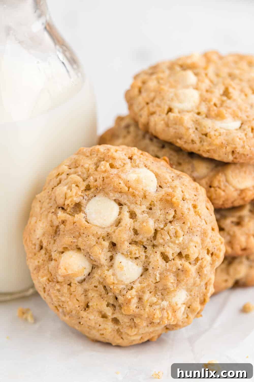 A stack of white chocolate oatmeal cookies beside a tall glass of cold milk, suggesting a perfect snack.