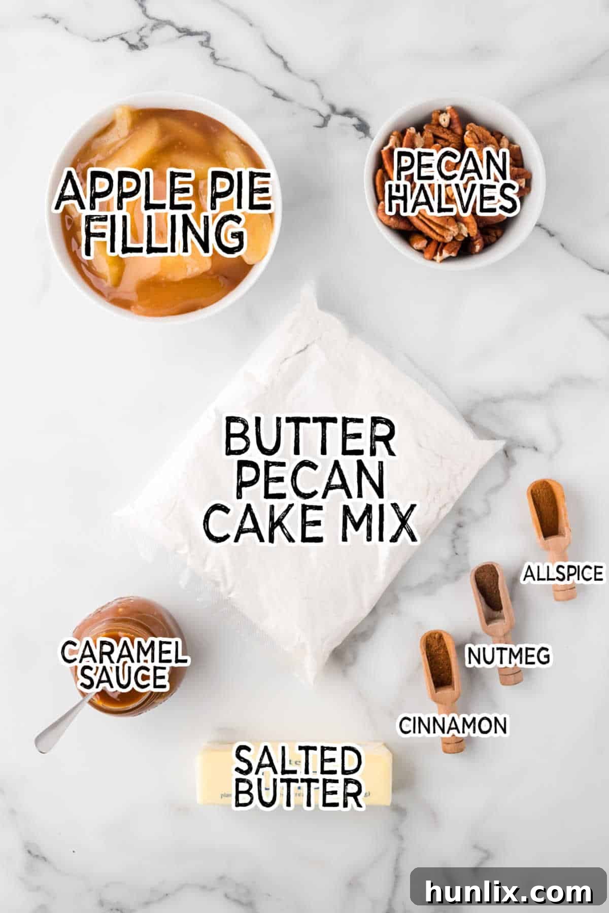 Effortless Caramel Apple Delight 3 A flat lay of all the ingredients needed for caramel apple dump cake on a white marble background, including cake mix, apple pie filling, caramel sauce, spices, butter, and pecans.