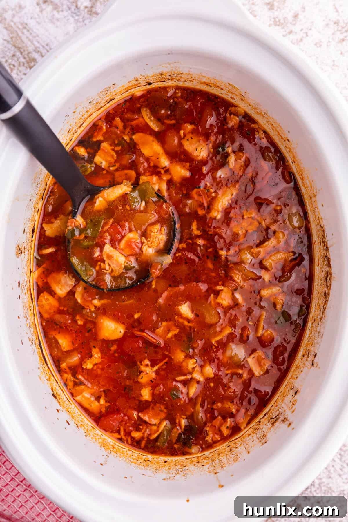 Pizza soup in a white slow cooker with a ladle, garnished with fresh basil.