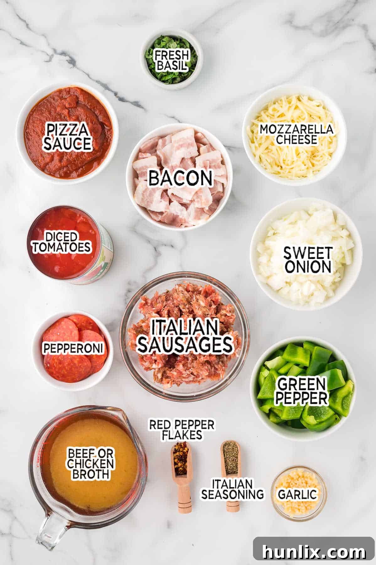 A selection of fresh ingredients including Italian sausage, bacon, pepperoni, diced tomatoes, broth, spices, onion, garlic, and green pepper arranged on a marble counter.