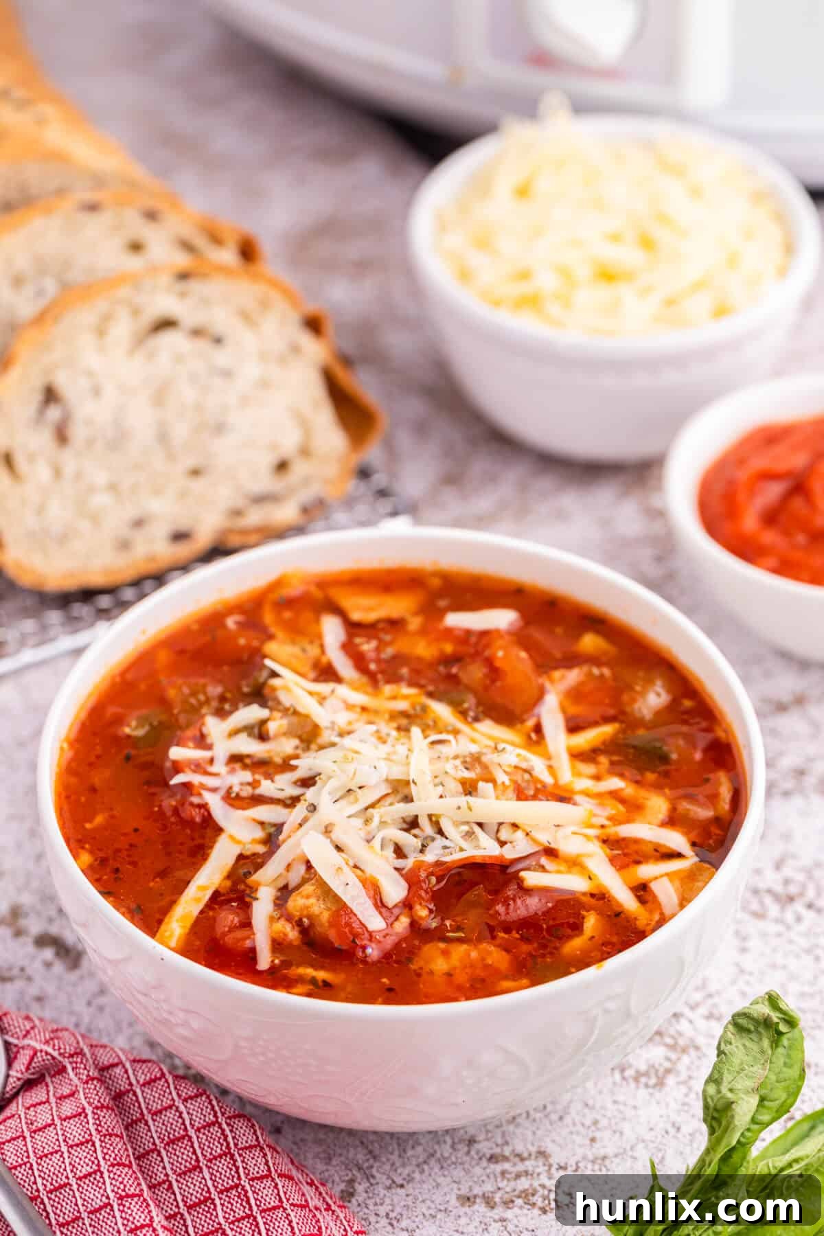 A bowl of rich pizza soup, garnished with melted cheese and fresh herbs, ready to be enjoyed.