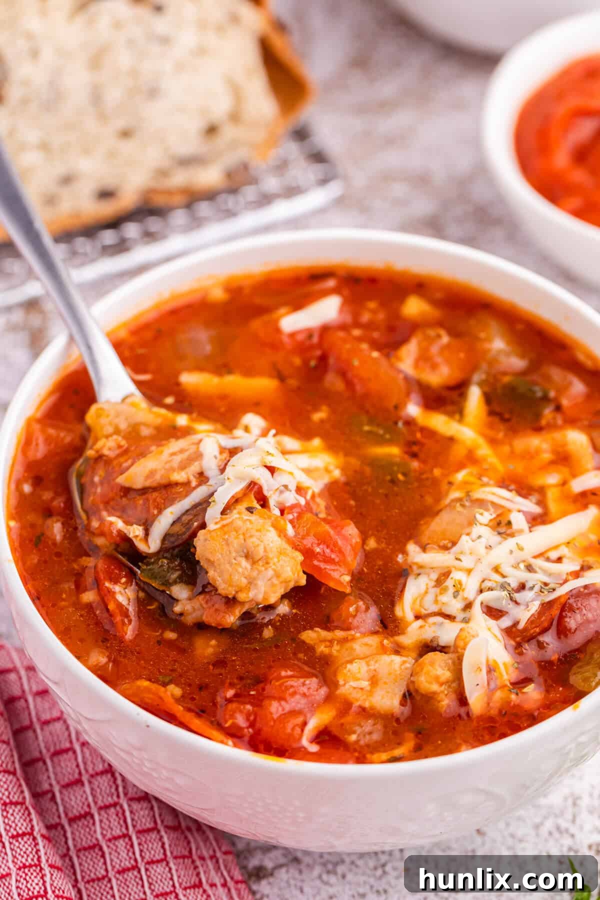A spoonful of delicious pizza soup being lifted from a bowl, showcasing the melted cheese and hearty ingredients.