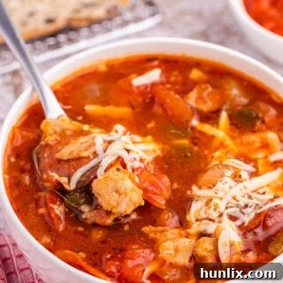 A bowl of delicious pizza soup with a spoon, showing melted cheese and hearty ingredients.