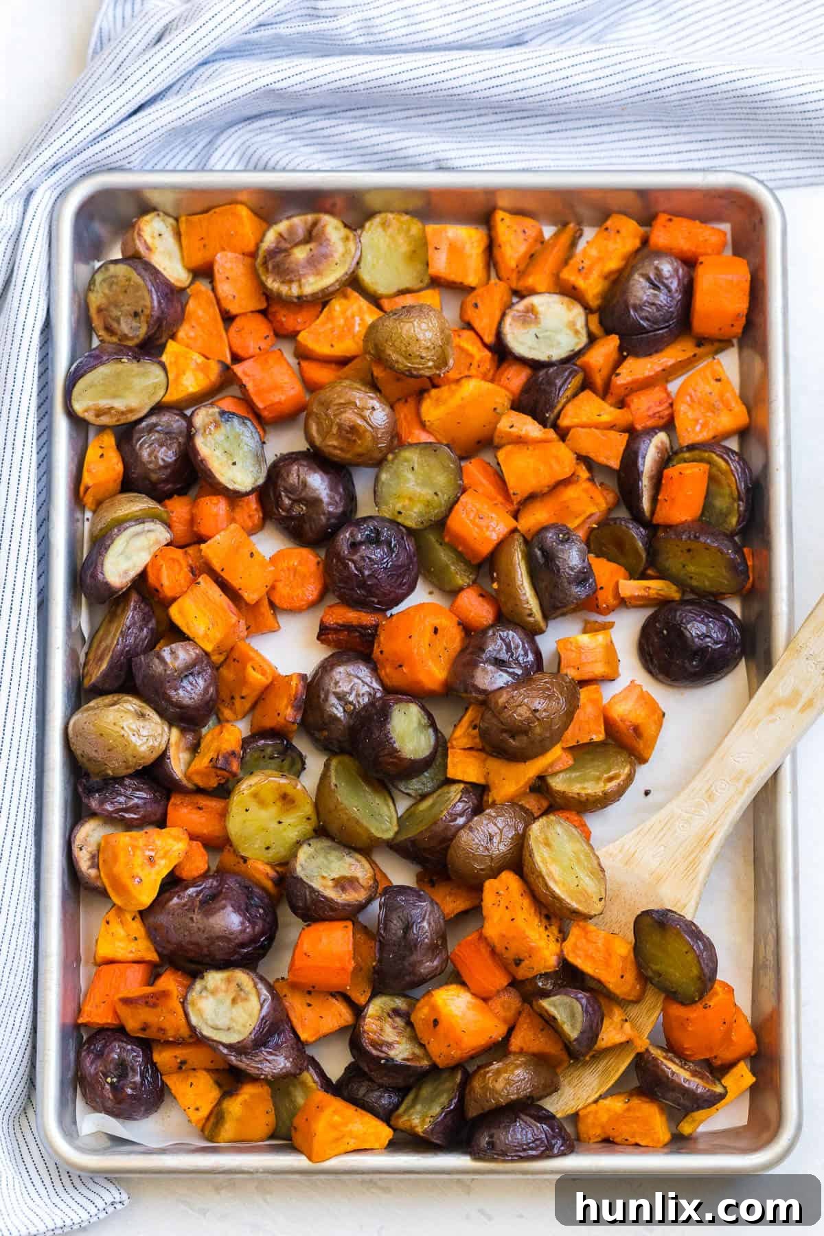 Roasted root vegetables on a sheet pan with a wooden spoon.