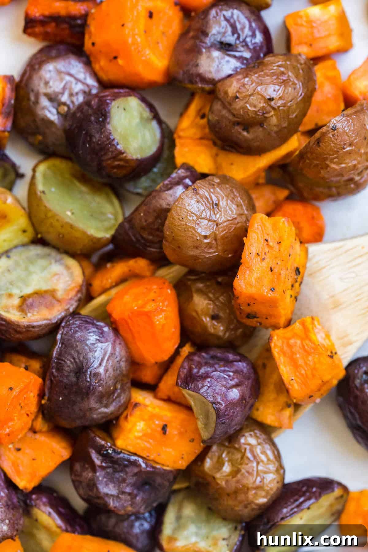 Roasted root vegetables on a sheet pan with a wooden serving spoon.