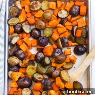 Roasted root vegetables on a sheet pan with a wooden spoon.