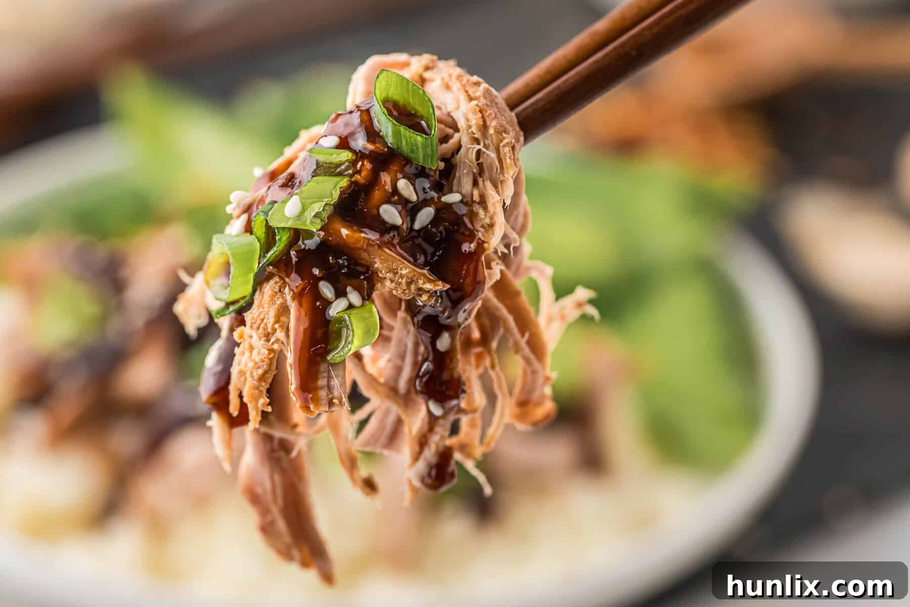 Soy Ginger Pork Tenderloin 9 Shredded Asian pork tenderloin held by wooden chopsticks, emphasizing its tenderness.