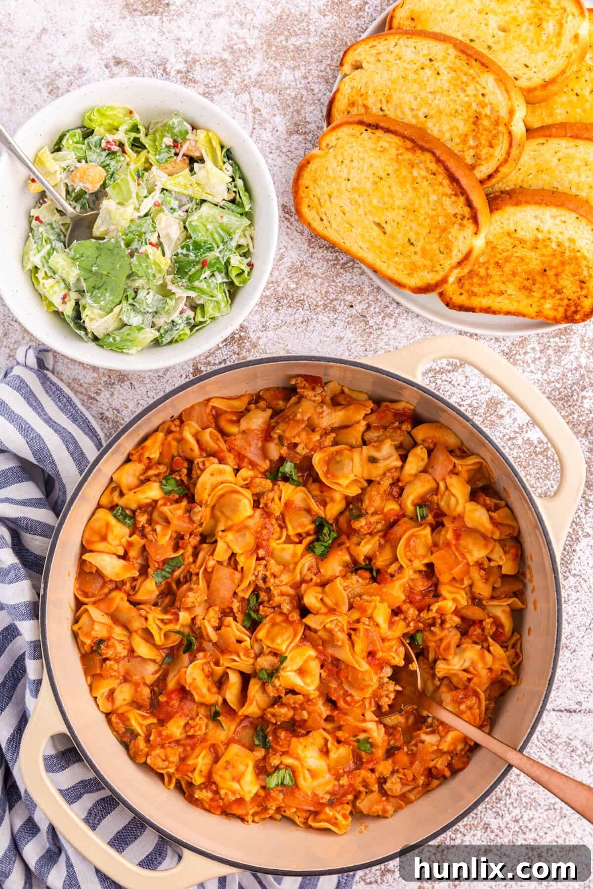 A large Dutch oven filled to the brim with creamy One-Pot Sausage and Cheese Cappelletti, garnished with fresh basil leaves, ready to be served.