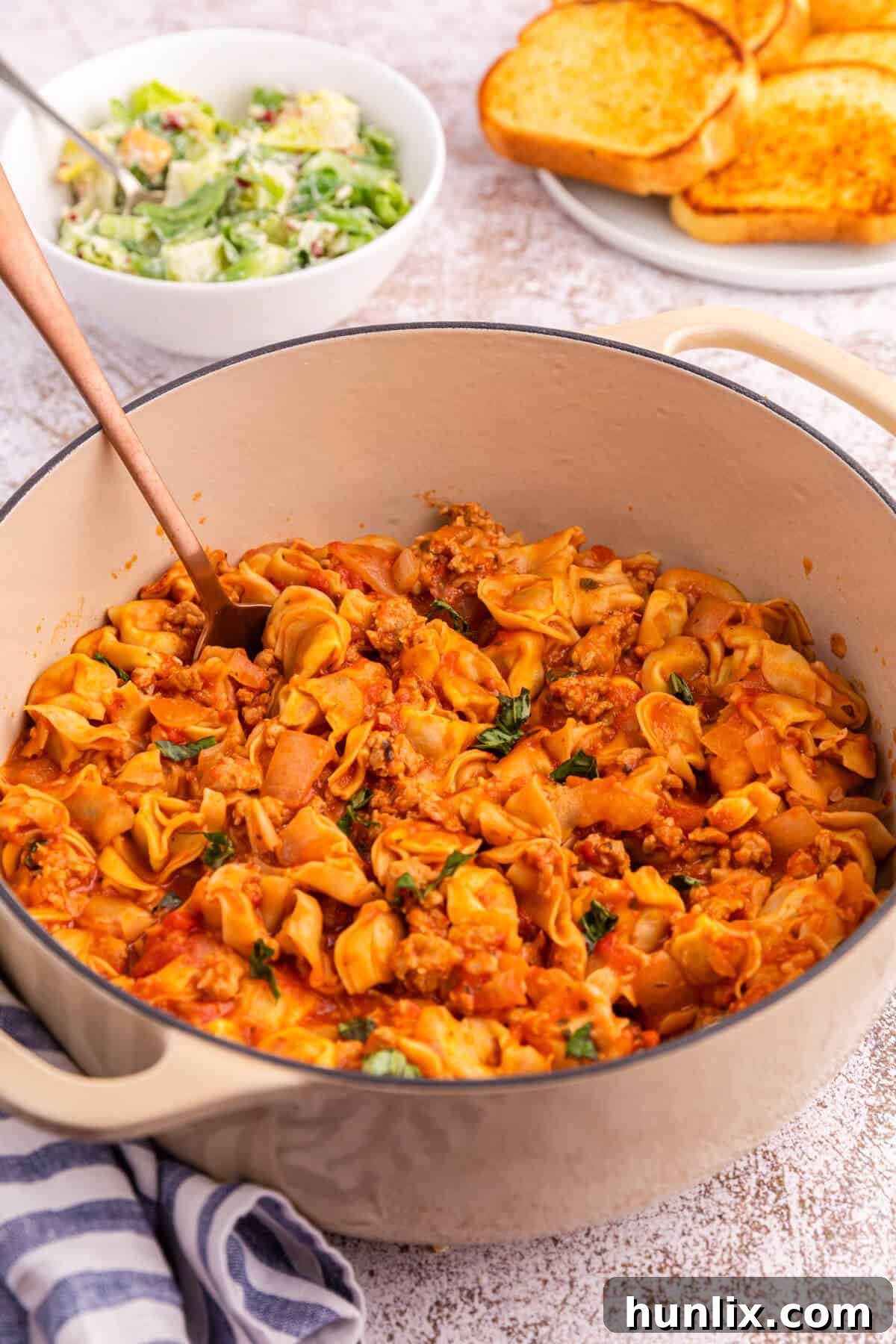 A serving spoon lifting a generous portion of One-Pot Sausage and Cheese Cappelletti from a Dutch oven, showcasing the melted cheese and flavorful sauce.