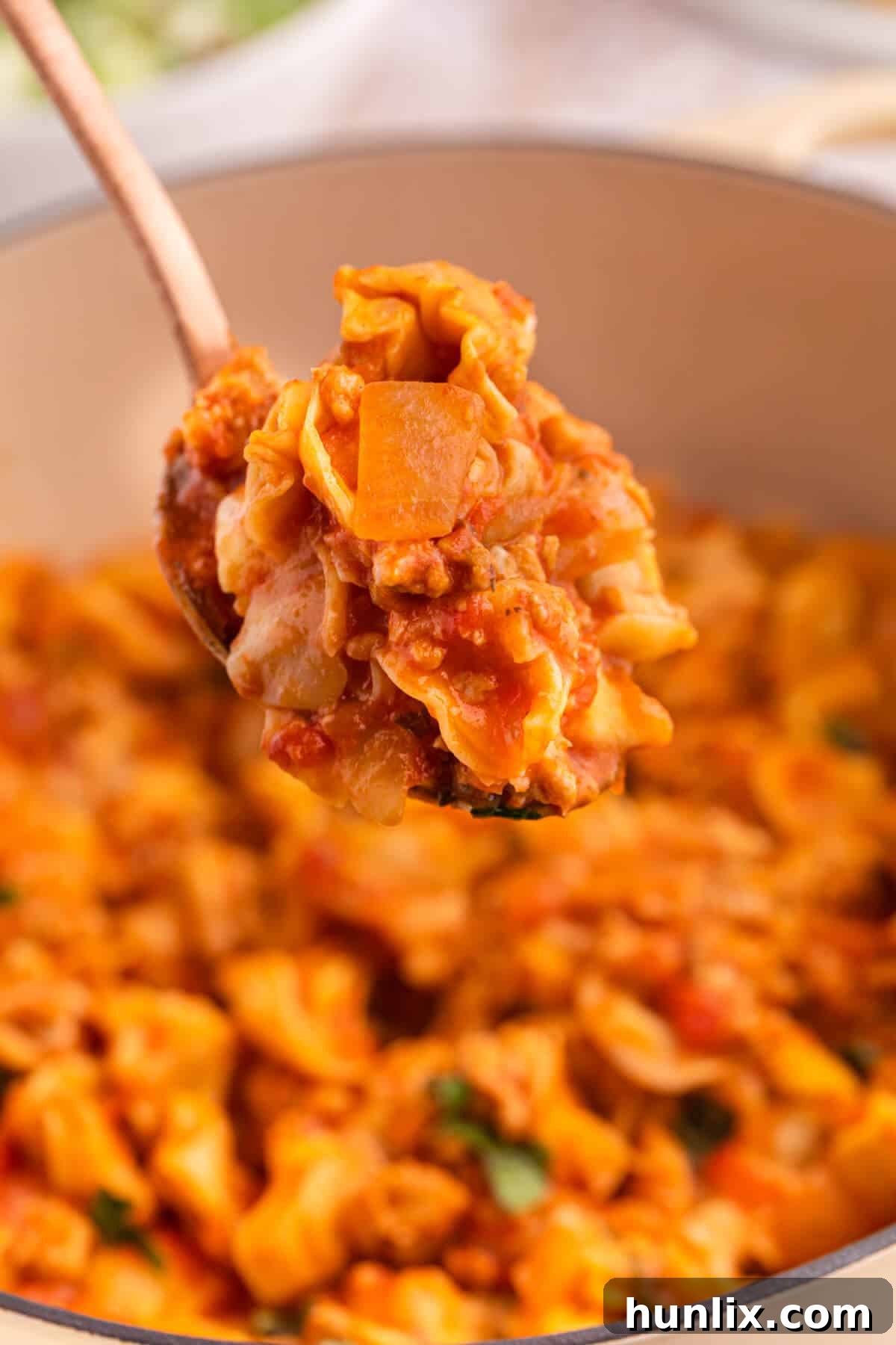 A close-up of a serving spoon filled with One-Pot Sausage and Cheese Cappelletti, showcasing the perfectly cooked pasta, savory sausage, and melted cheese, ready for enjoyment.