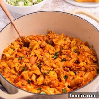 A Dutch oven of sausage and cheese cappelletti with a serving spoon.